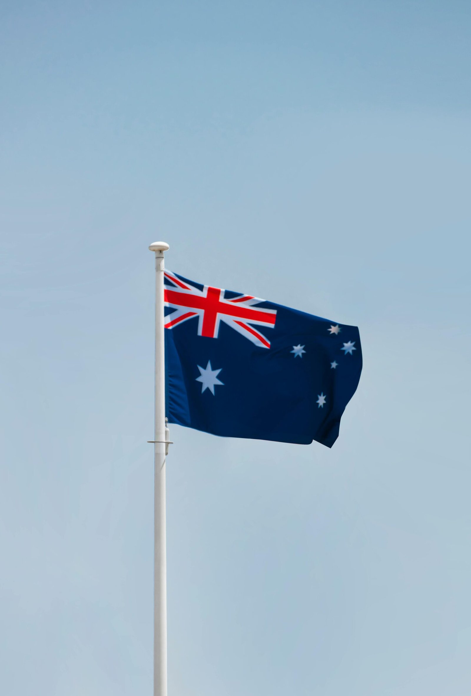 The Australian national flag flying high against a blue sky in Canberra.