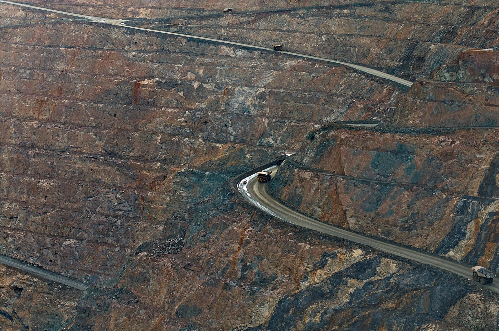 Aerial view of open-pit mine with haul trucks navigating winding roads.